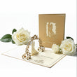 The 3D Pop-Up Wedding Card – Gold Bridal Couple Greeting Card for Weddings, Anniversaries & Invitations, featuring a couple silhouette on a white background with white roses.