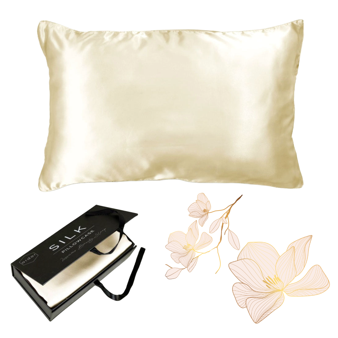 The Ardor Mulberry Silk Standard Pillowcase Ivory Dreams displayed alongside its packaging and a decorative flower, suggesting a luxurious and elegant product intended for comfort and style in bedroom decor.