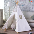 The Giant Teepee Playhouse Tent in Natural Canvas texture, set up indoors. It features wooden poles and a flap door, with a small plush toy inside.