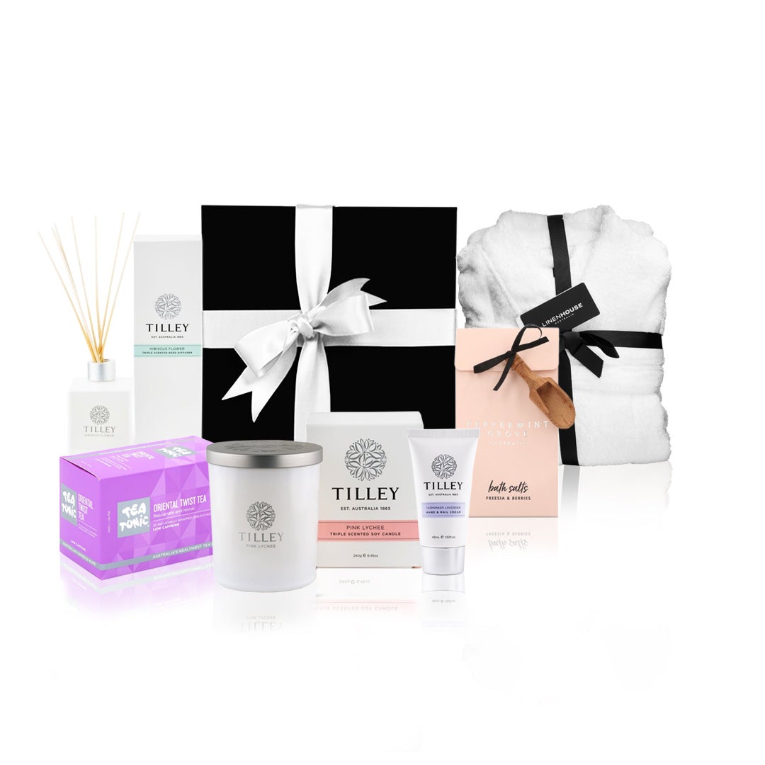 A Luxury Self Care Gift Hamper featuring Tilley branded products including a reed diffuser, soy candle, hand & nail cream, bath salts, and tea tonic, all presented in a black box with a white bow and an additional linen house robe.