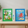 The Magic Water Colouring Books Kids 2 Pack – Reusable Animals & Sea World Mess-Free Drawing Set featuring two children's books titled 'Magic Water Book' with animal and ocean-themed illustrations on a wooden surface.