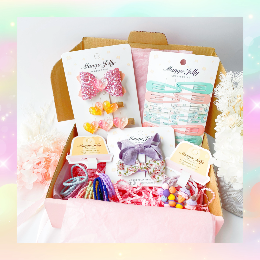 The Mango Jelly Kids Surprise Hamper Box - Small, a pink surprise hamper box opened to reveal various colourful children's hair accessories like hair clips and scrunchies.