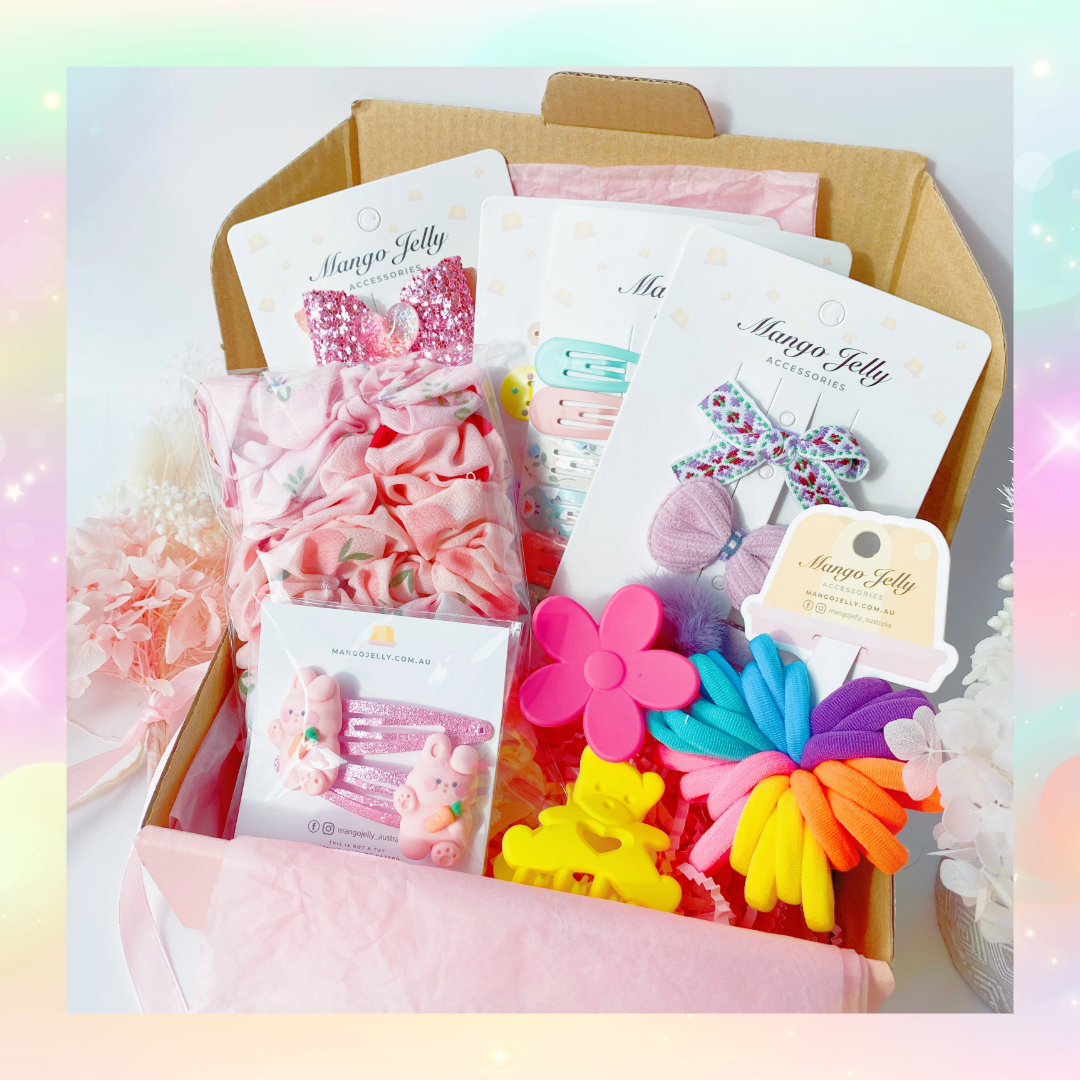 The Mango Jelly Kids Surprise Hamper Box - Jumbo, a pink surprise hamper box opened to reveal various colourful children's hair accessories like hair clips and scrunchies.