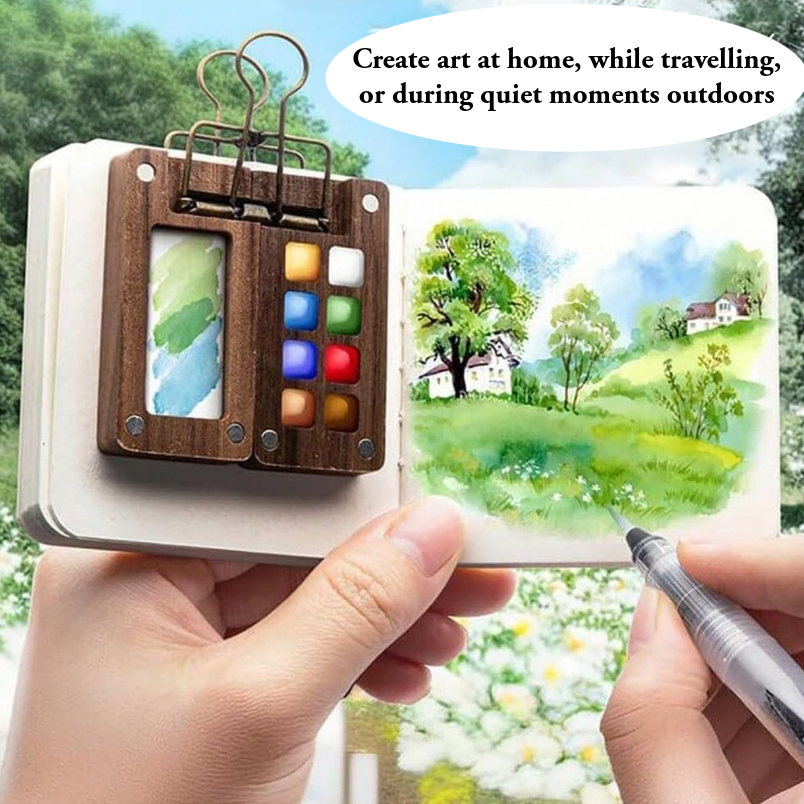 Hand holding a small art kit with watercolour paints and a sketchbook, set against a scenic background.