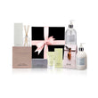 A Peppermint Grove Pamper Hamper gift set including a variety of skin care products, such as hand and body wash, cream, soap bar, and a room diffuser, all presented in a black box with a pink bow. 
