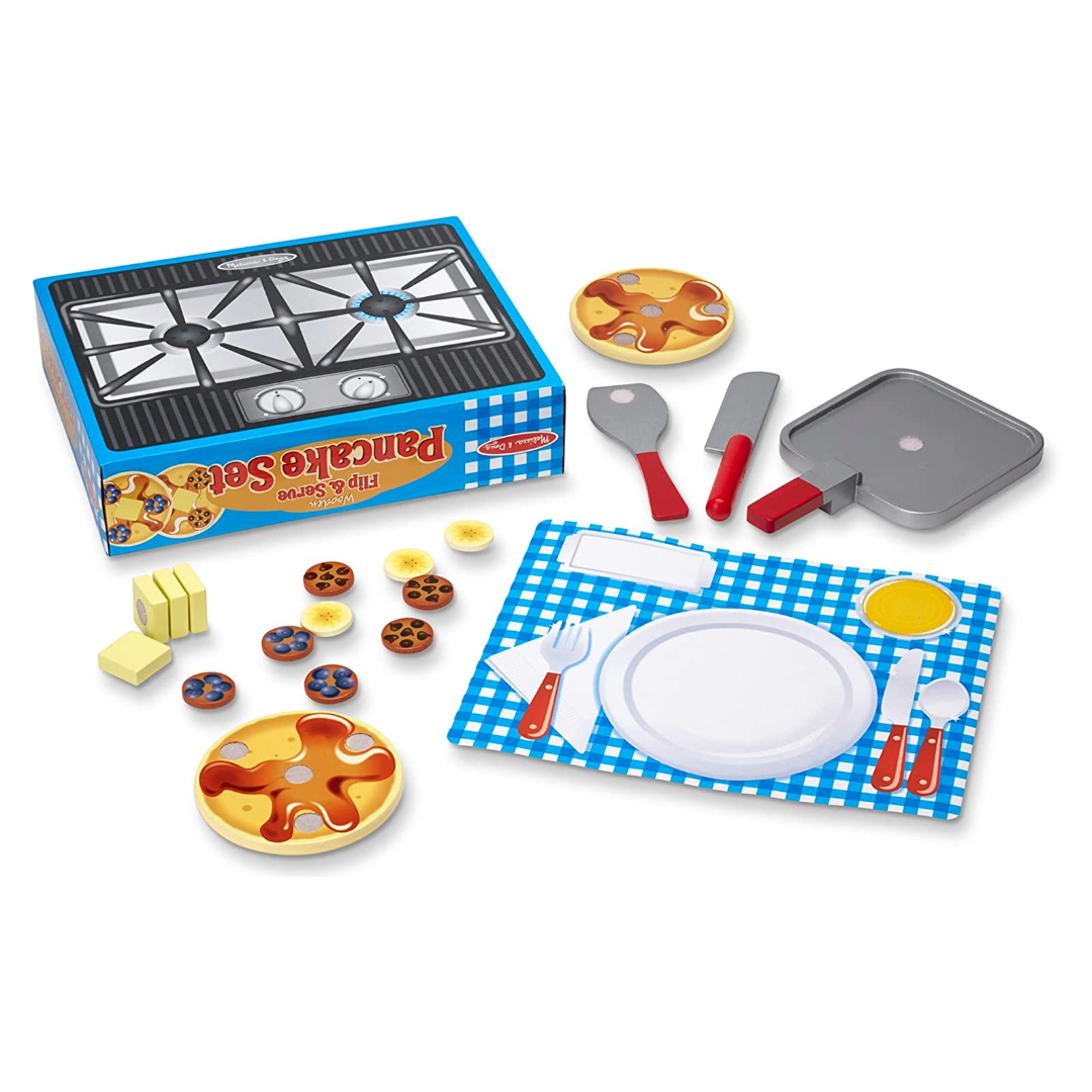 The Wooden Flip and Serve Pancake Set - 19 Piece Breakfast Play Set including two pancakes with toppings, a wooden skillet, knife, and spatula, all displayed on a blue and white checkered play table surface with a box in the background.